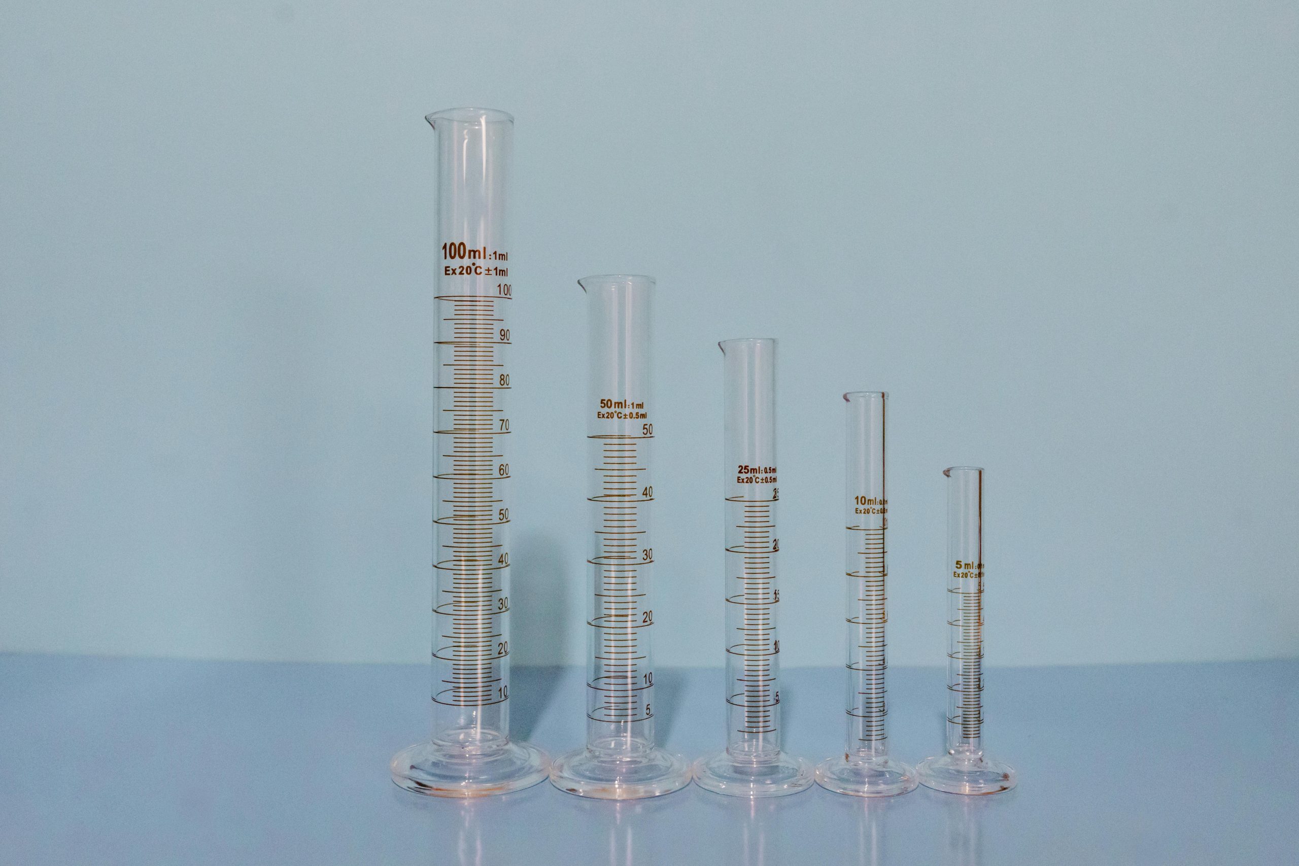 Offerings A variety of graduated cylinders in different sizes on a blue surface, ideal lab equipment image.